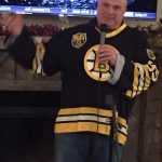 Individual wearing a Bruins jersey speaks into microphone facing the camera