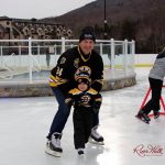Individual poses for the camera smiling with a small child wearing Bruins attire and hockey skates.