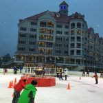 People skate around an ice rink outside the RiverWalk hotel at dusk in the snow.