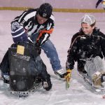 Two youths sit in sled hockey sleds talking to the referee. Snow is falling.