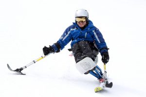 An individual is seated in a monoski, skiing using one ski and two outriggers.