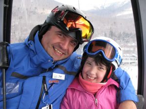 A ski instructor and young participant smiling on a gondola ride up the mountain.