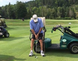 Individual utilizes a putter while standing with the assistance of a Solo-Rider golf cart. 