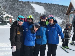 Five skiers smiling for a picture in front of ski slopes. 