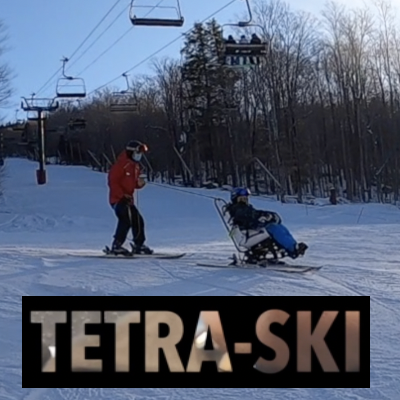 An individual is seated skiing in a tetra-ski while a coach skis behind, holding a tether attached to the tetra-ski’s frame.