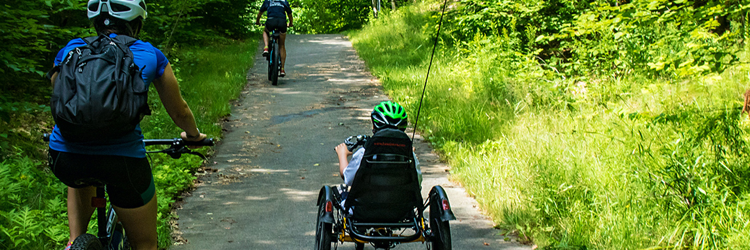 Two individuals on upright bikes and one individual on a recumbent bike riding down a bike path.